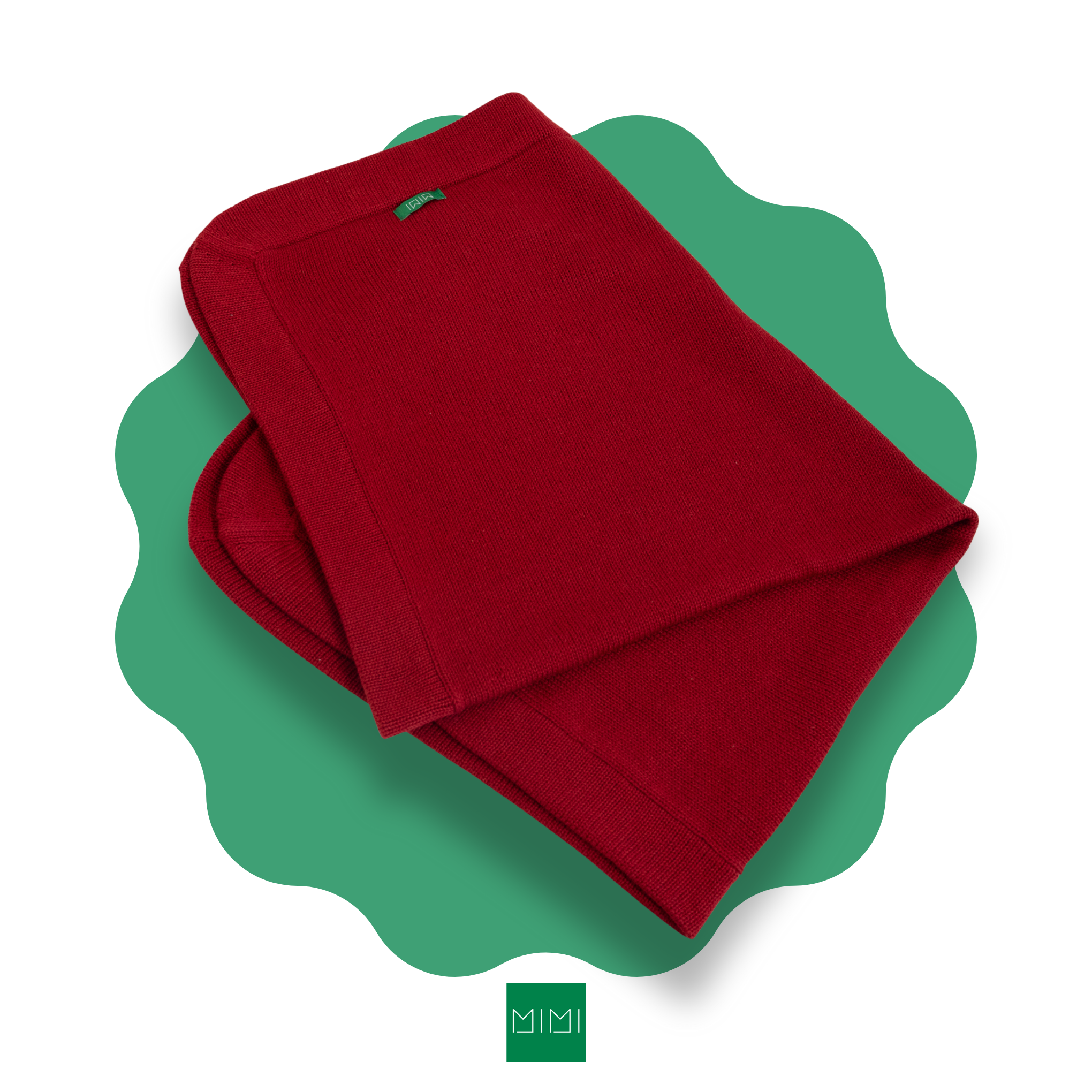 Folded red knit newborn blanket on a green scalloped mat with 'MIMI' brand logo