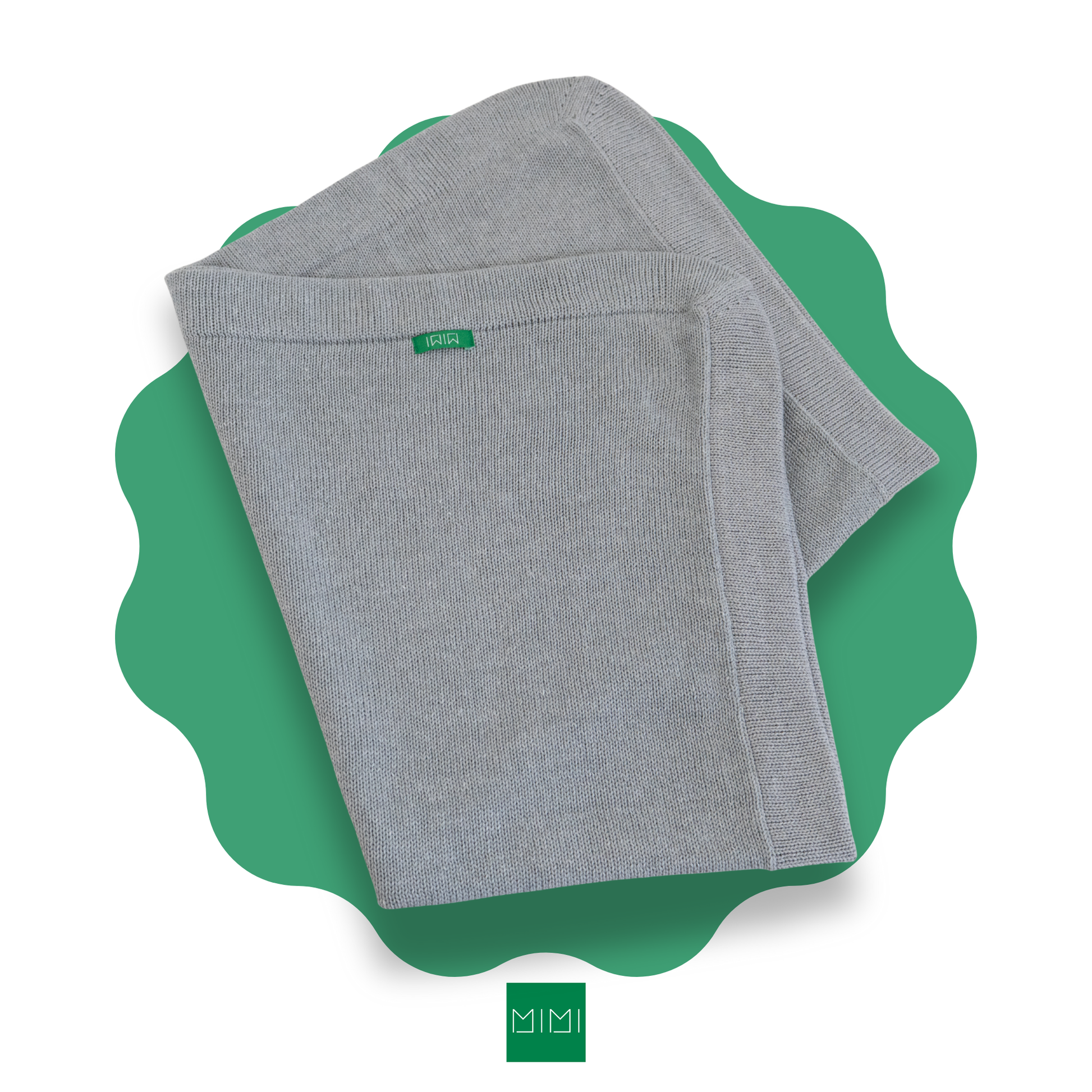 Folded grey knit newborn blanket on a green scalloped mat with 'MIMI' brand logo